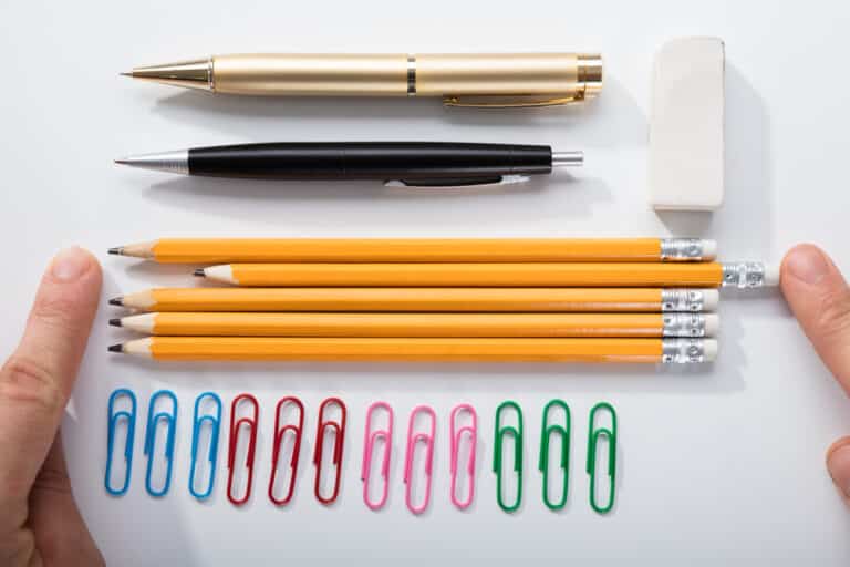 Office supplies neatly arranged on white surface, hands putting pencils in line